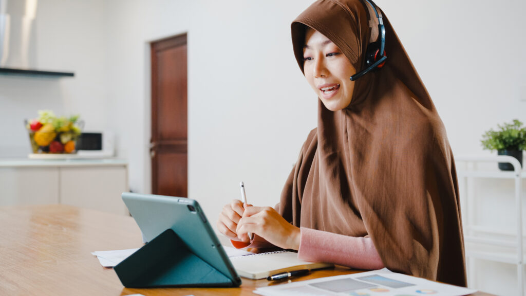 Asia muslim lady wear headphone using digital tablet talk to col